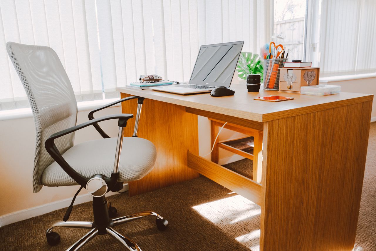 about-us-01 A modern office workspace featuring a wooden desk, chair, laptop, and bright natural light.