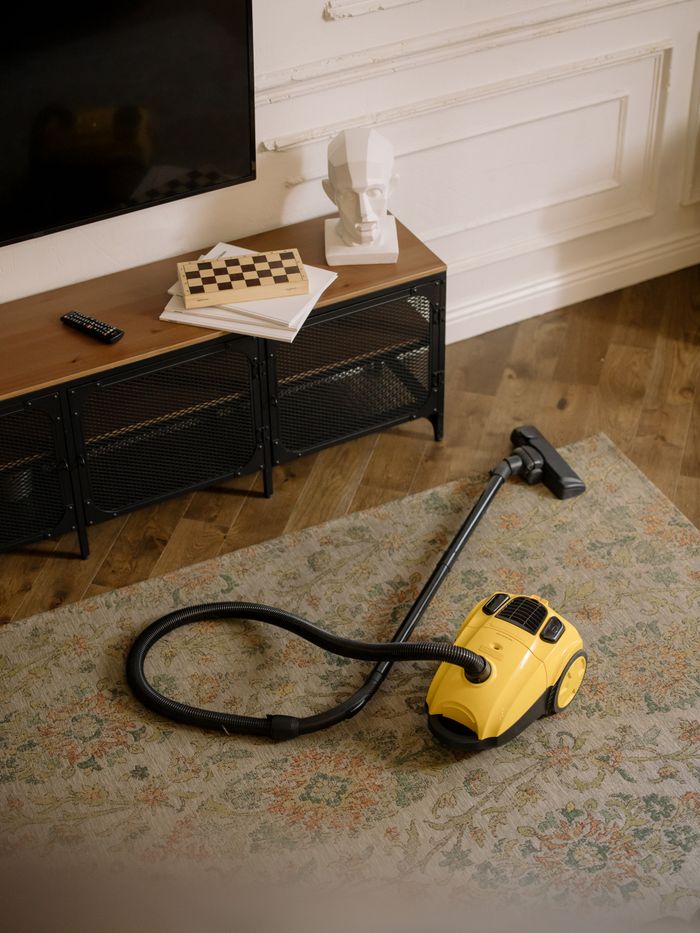 how-we-are A stylish living room with a yellow vacuum cleaner on the rug, showcasing home cleanliness.