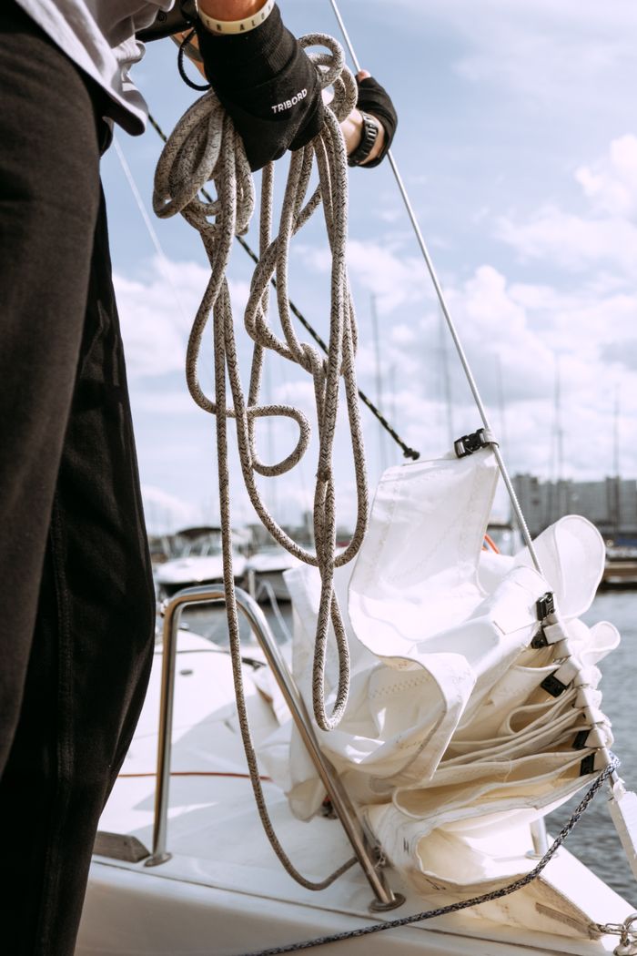 Close-up of a sailor coiling rope on a yacht, preparing for a sailing trip at marina.